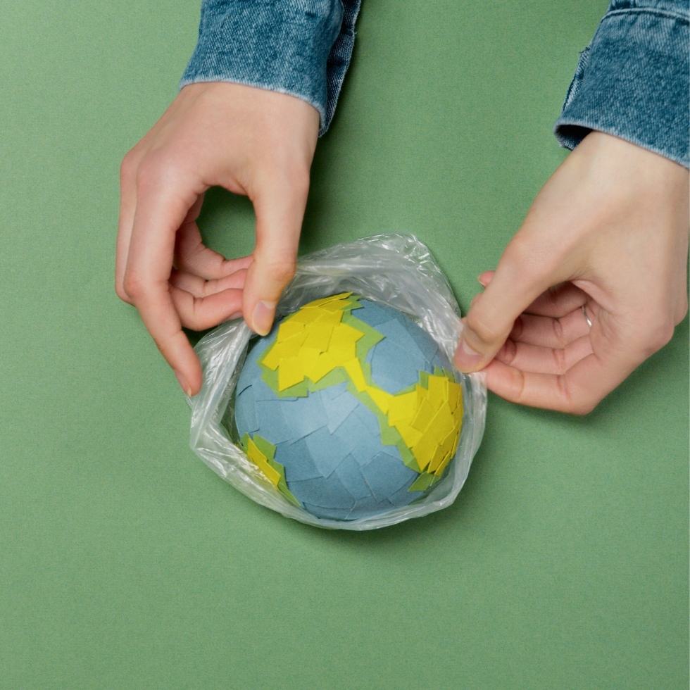 Lehrerinnenhände halten Weltkugel aus Papier in Plastik
